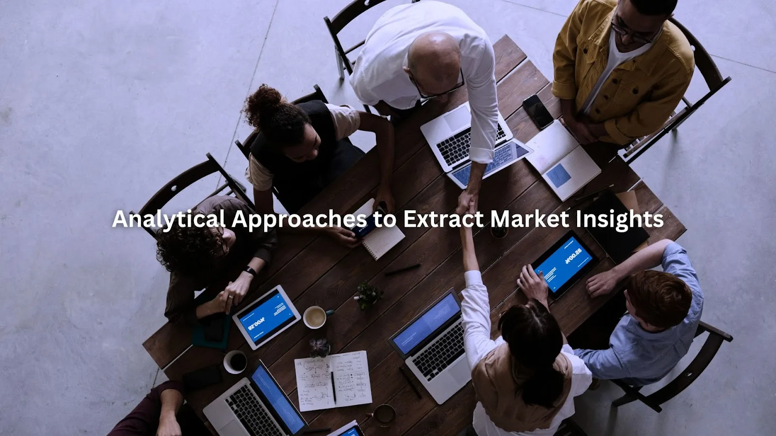 Team collaborating around a table with laptops and tablets, focusing on data driven market insights.