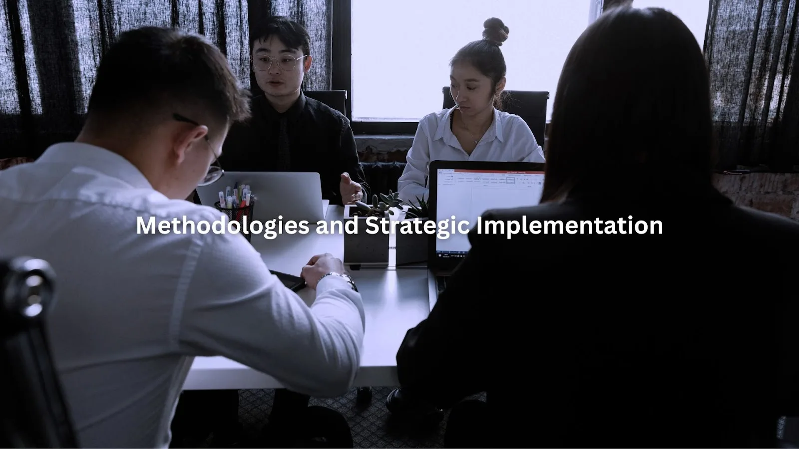 Four business professionals engaged in a strategy meeting at a conference table with laptops, discussing methodologies and implementation plans.