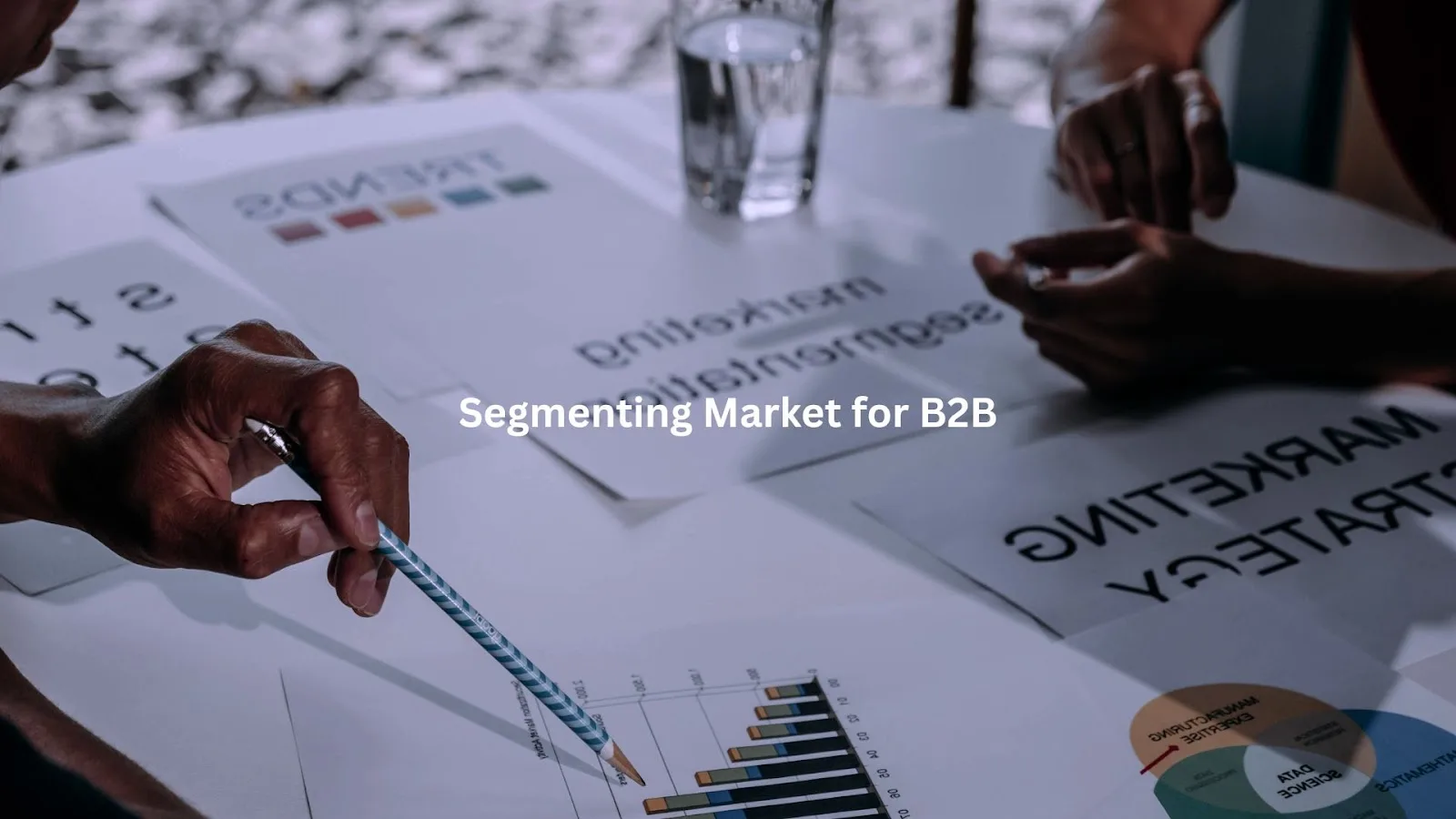 Hands analyzing segmentation data for B2B market targeting, surrounded by financial charts and graphs on a desk.